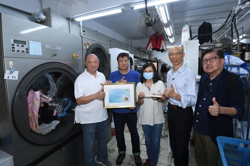 支持環保:  黃錦星（右二）到訪受惠於洗衣業抗疫資助計劃的洗衣店。該洗衣店支持香港發展可再生能源，店鋪負責人展示其購買的本地可再生能源證書。